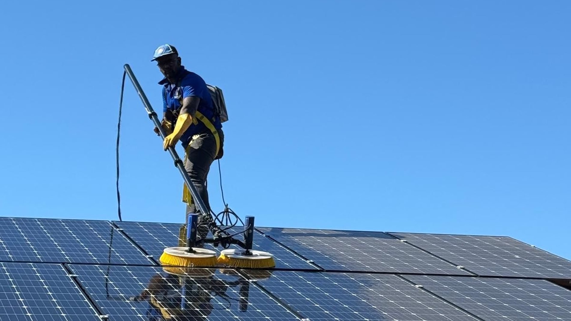 Technician brushing rooftop solar panels with a rotating brush