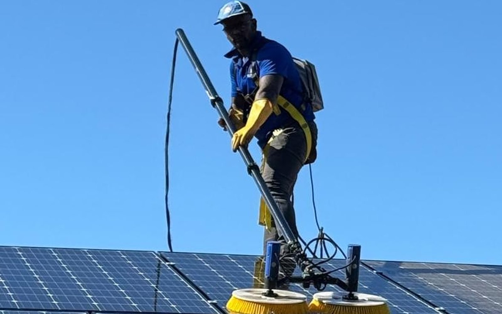 Technician brushing rooftop solar panels with a rotating brush